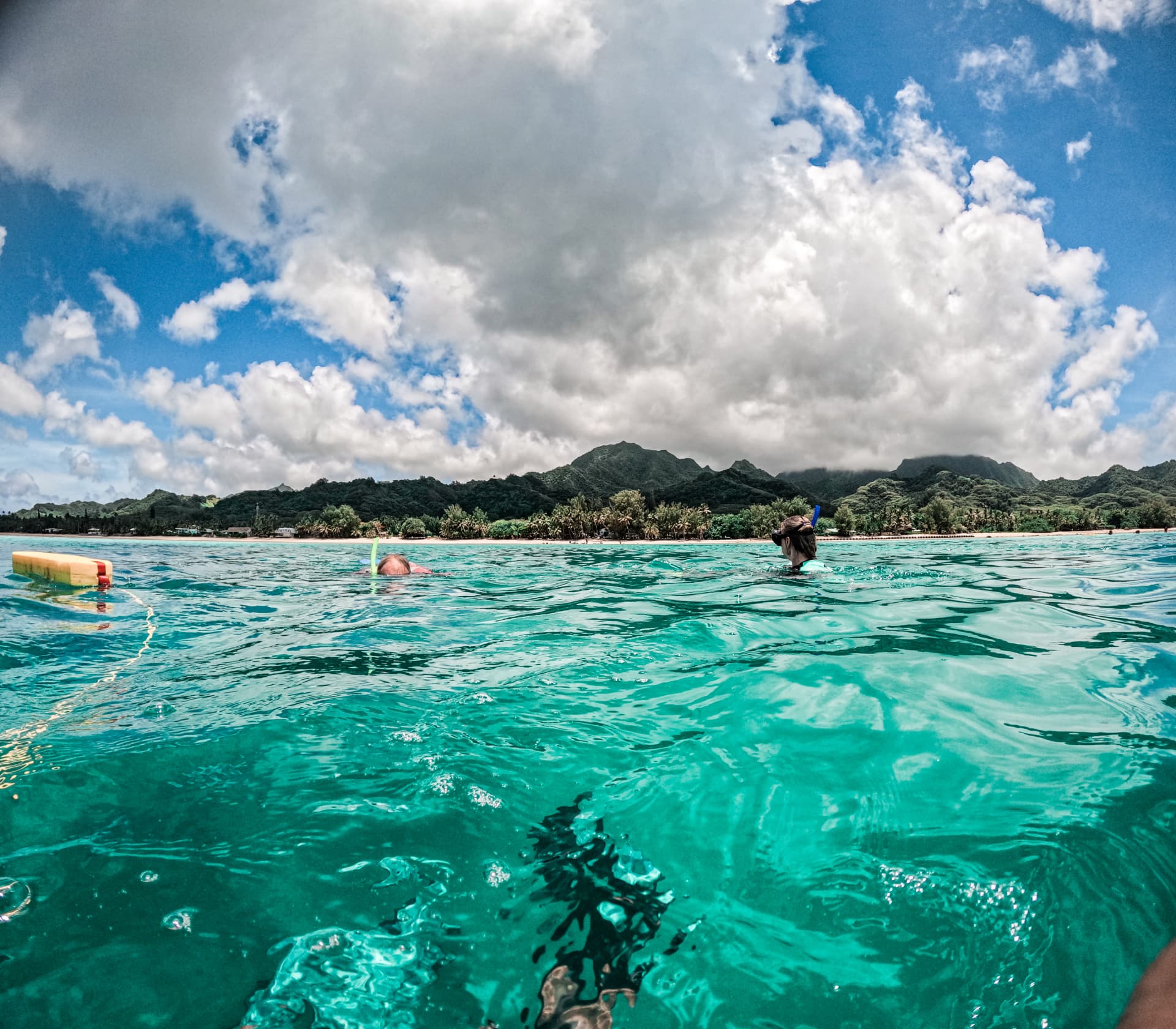 Snorkellers floating in the lagoon with Rarotonga's green peaks behind