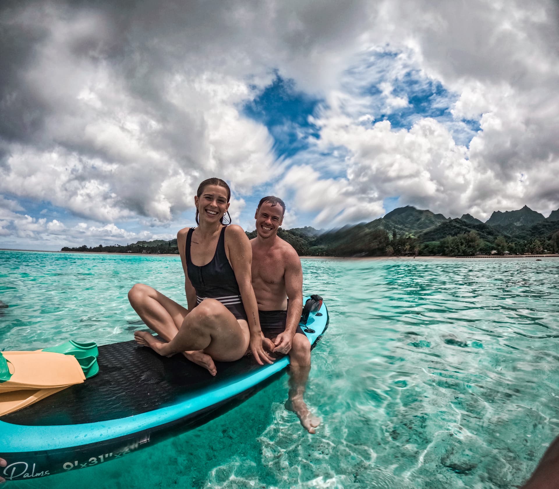 Two guests sitting on a paddleboard in the clear Rarotonga lagoon